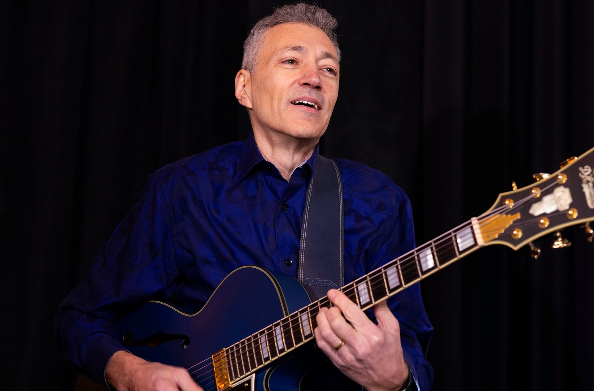 Jazz guitarist Vinny Valentino smiling as he plays a blue archtop guitar